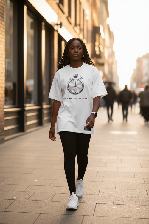 A woman walking down a city street wearing a white graphic t-shirt with a circular clock design and the text 'NO TIME FOR EXCUSES' | From Me Fitness Apparel