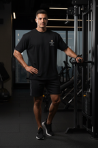 Man in a gym wearing a black t-shirt and shorts, standing in front of gym equipment | From Me Fitness Apparel