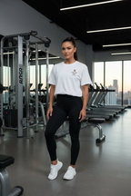 Woman in a gym wearing a white t-shirt with a logo and black leggings | From Me Fitness Apparel