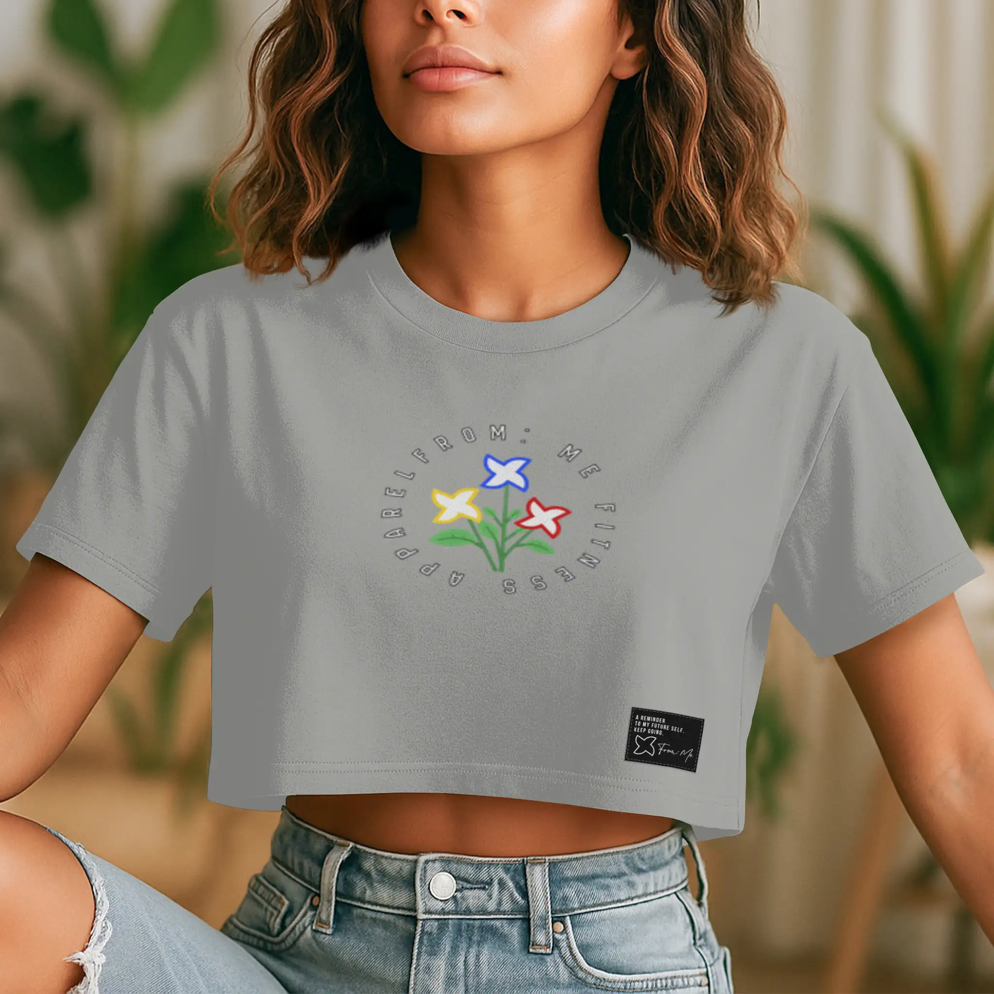 Person wearing a gray crop top with a colorful flower design and text, sitting outdoors.