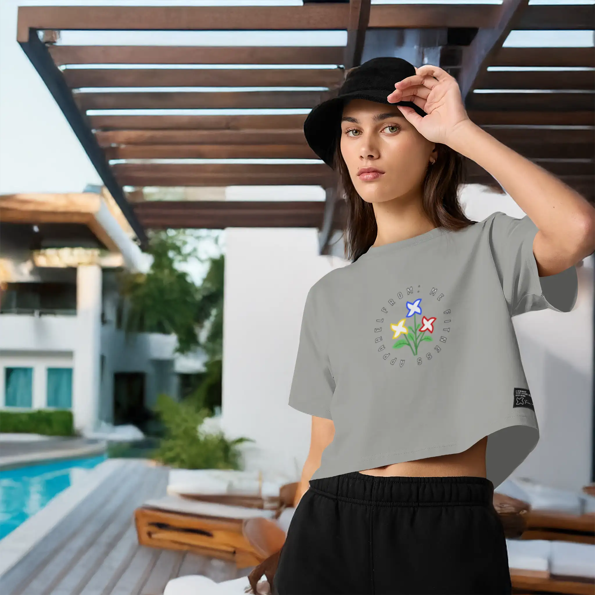 Woman wearing a gray t-shirt with text and black shorts, standing outdoors near a pool.