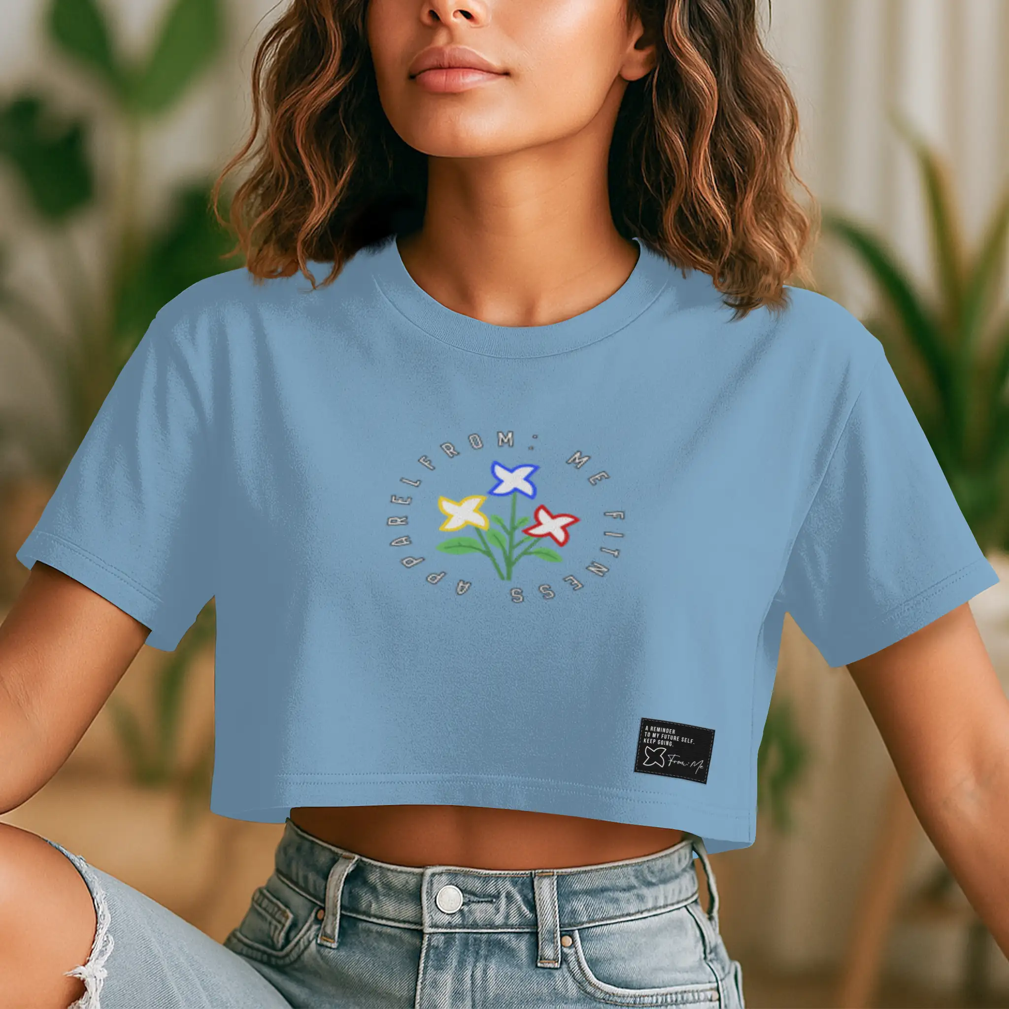 Person wearing a blue crop top with floral design and text, sitting outdoors | From Me Fitness Apparel
