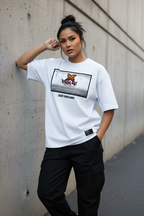 A woman wearing a white graphic t-shirt and black cargo pants, leaning against a concrete wall in an outdoor urban setting.